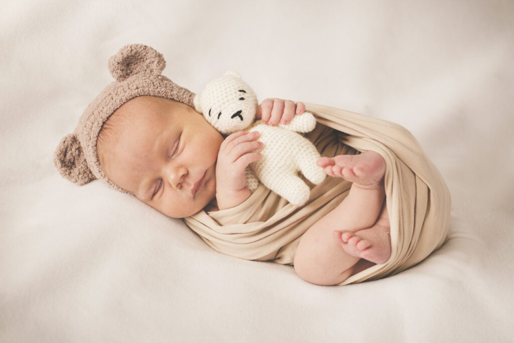 Newborn Baby in Neutral Outfit with Bear Hat and Stuffed Bear